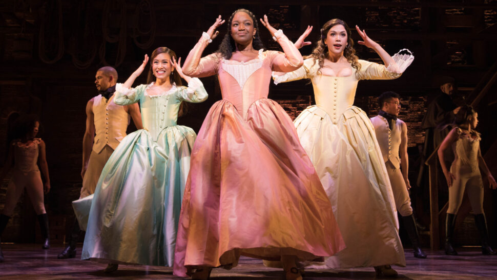 Female actors perform in Hamilton in period costumes.